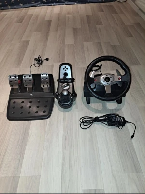 Logitech G25 Racerratt med tillhörande pedalenhet och separat växelspak  - Logitech G25 racerratt med tillhörande pedalenhet och separat växelspak. Ratten har läderklätt rattkrans, växelpaddlar bakom ratten samt knappar på framsidan. Pedalenheten har tre pedaler för gas, broms och koppling. Växelspaken är en fristående enhet med H-mönstrad manuell växling och flera funktionsknappar. Utrustningen ansluts med kabel. Passar för bil- och racingspel som stödjer Logitech G25. Frakten betalas av köparen. Pris kan diskuteras