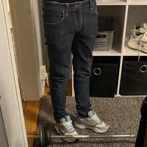 Mörkblå slim fit jeans från Nudie Jeans - Säljer ett par mörkblå slim fit jeans från Nudie Jeans med klassisk femficksmodell och kontrastsömmar. Jeansen har normal midja och är tillverkade i stretchig denim för skön passform. Perfekta till sneakers eller boots. W31 mer som 29-30