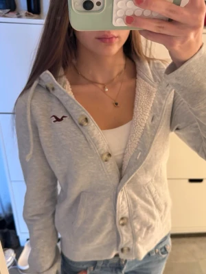 Fodrad hollister hoodie med knappar - Vintage grå Hollister-hoodie med foder och knappar. Storlek L, passar bättre som S. Mycket gott skick, fodret är lite missfärgat som du kan se. Har Hollister-fågeln loggan på bröstet. Följ för fler liknande kläder och köp gärna bundle/paket!