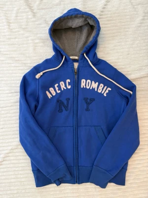 Vintage Abercrombie & fitch zip up hoodie - Vintage blå Abercrombie & Fitch-hoodie med dragkedja för män. Storlek S! Har Abercrombie & Fitch-loggan på bröstet. Mycket bra skick, men den vita loggan har blivit lite rosa/missfärgad – inget som märks särskilt mycket. Följ för fler liknande kläder och köp bundle!