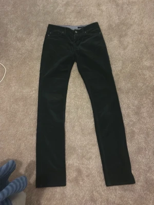 Svarta manchesterbyxor Tommy Hilfiger - Snygga lågmidjade mörk gröna manchesterbyxor från Tommy Hilfiger med klassisk rak passform och diskreta fickor fram och bak. Byxorna har en mjuk och skön manchesterstruktur som ger en cool vintagekänsla. Perfekta för dig som vill ha en stilren och tidlös look.