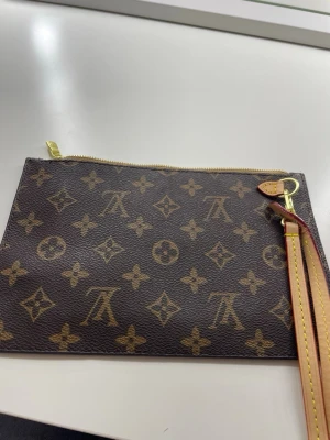  Kuvertväska - Snygg kuvertväska från hm  i klassiskt brunt monogrammönster med guldfärgad dragkedja och avtagbar handledsrem i läder. Insidan är beige med bruna ränder och har en liten ficka. Perfekt för att bära det viktigaste med stil.