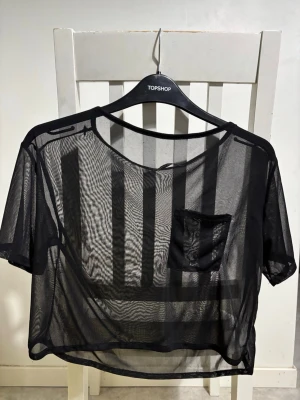 Genomskinlig svart T-shirt  - Svart genomskinlig T-shirt med ficka framtill. 