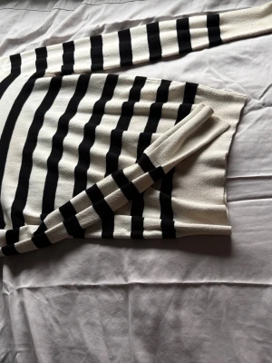 Randig stickad tröja från Zara - Säljer en snygg stickad tröja från Zara i krämvitt med svarta horisontella ränder. Tröjan har rund halsringning och långa ärmar. Perfekt för dig som gillar klassisk och stilren design.