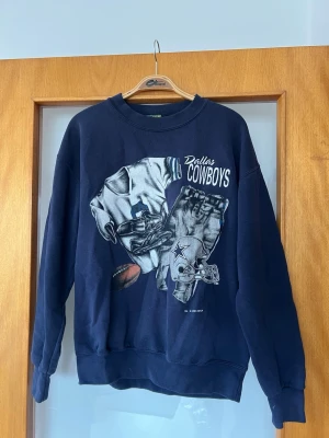 Dallas Cowboys sweatshirt blå - Mörkblå sweatshirt med stort Dallas Cowboys-tryck framtill. Tröjan har rund hals, långa ärmar och ribbade muddar. 