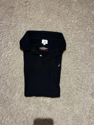 Marinblå pikétröja från Boomerang - Klassisk marinblå pikétröja från Boomerang med krage och knappar framtill. Tröjan har korta ärmar och en liten broderad logga på bröstet. Tillverkad i bomull för en bekväm känsla och snygg passform.