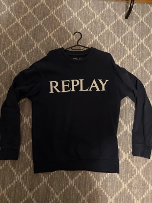 Mörkblå sweatshirt från Replay - Snygg mörkblå sweatshirt från Replay med stor vit logga över bröstet. Klassisk rund halsringning. Tillverkad i mjukt material som känns skönt mot huden. Perfekt för en avslappnad och trendig look.