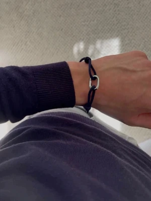 Marinblått armband med silverdetalj - Stilrent armband med marinblått snöre och en cool, silverfärgad metallögla som detalj. Perfekt accessoar för dig som gillar minimalistisk och modern stil. Justerbar knytning gör att det passar de flesta handleder.
