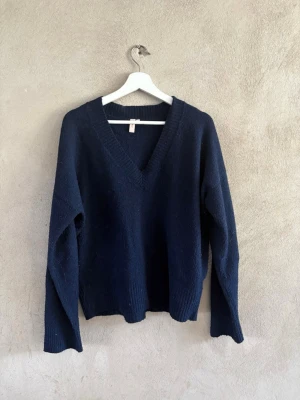 Mörkblå stickad tröja med v-ringning - Mysig mörkblå stickad tröja med djup v-ringning och långa ärmar. Tröjan har ribbstickade muddar vid ärmslut och nederkant. Perfekt för lager på lager och enkel att matcha med olika stilar.