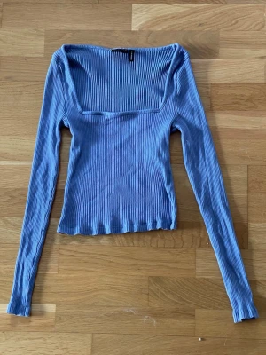 Lilablå ribbad topp med lång ärm från Asos Design i storlek 36 - Trendig lilablå ribbad topp med fyrkantig urringning och långa ärmar från Asos Design i storlek 36. Toppen har normal passform och är tillverkad i mjukt stretchigt material som sitter snyggt på kroppen. Perfekt att styla med jeans eller kjol för en cool look.