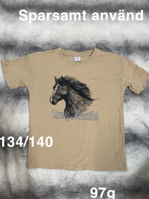  t-shirt med hästmotiv -  t-shirt med ett stort tryck av ett hästhuvud och texten 'Strong. Beautiful' på framsidan. Klassisk passform och rund halsringning. Perfekt för dig som gillar hästar och vill ha en unik t-shirt i garderoben.🌸 Sparsamt använd. Storlek 134/140 