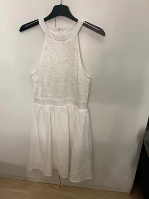 Vit spetsklänning med ärmlös design - Söt vit klänning med spetsdetaljer på överdelen och slät kjol. Klänningen är ärmlös med hög halsringning och har en feminin, luftig känsla. Perfekt för sommarens alla tillfällen och studentfirande. Använd enbart 1 gång på min konfrontation för 4 år sen 