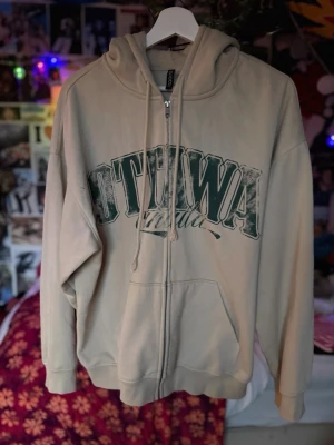 Ottawa Beige ziphoodie - beige hoodie med dragkedja från H&M. Stor grön text 'OTTAWA' på framsidan och fickor på sidorna.               ‼️Fråga om mått/hur den ser ut på‼️