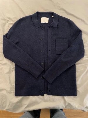 Mörkblå cardigan från Jack & Jones - Mysig mörkblå cardigan från Jack & Jones med klassisk krage, knäppning framtill och en bröstficka. Tillverkad i mjukt stickat material som passar perfekt till lager på lager. Enkel och stilren design som funkar till det mesta. Storlek XS, Modellen är 177 cm och 72 kg  