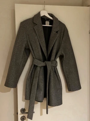 Grå kappa med bälte  - Grå kappa från ONLY med bälte i midjan. Väldigt fin passform. Storlek: M Fint skick. På mig som är ca 185 cm sitter den lite kortare, men på någon som är kortare blir den mer normal i längden.  Pris: 250 kr, har du förslag på pris kom med prisförslag.  Skickar inom 1 dag☺️✨