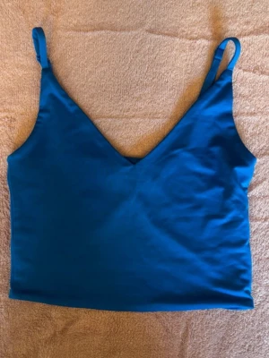 Blå linnetopp med smala axelband - En stilren blå linnetopp med smala justerbara axelband och v-ringning. Perfekt till sommaren och enkel att matcha med både jeans och kjol. Toppens material känns mjukt och följsamt mot huden.