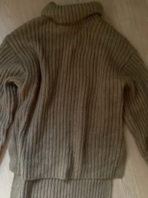 Brun stickad polotröja - Säljer en brun ribbstickad polotröja med lång ärm och hög krage. Tröjan har en avslappnad passform och är perfekt för lager på lager. Materialet känns mjukt och mysigt, och den ribbade strukturen ger en snygg look.