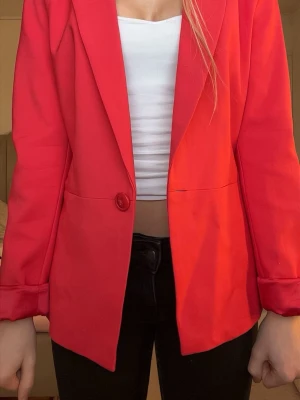 Röd kavaj med knapp - Snygg röd kavaj, med en knapp framtill och klassisk krage. Kavajen har långa ärmar med uppvikta muddar och är tillverkad i ett slätt tyg som ger en stilren look. Perfekt för att lyfta vilken outfit som helst.