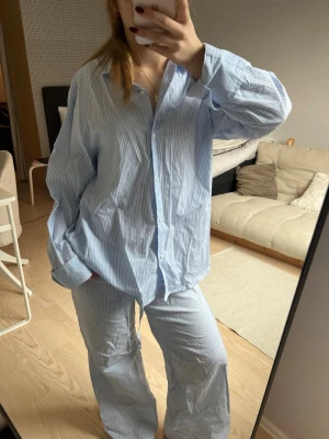 Blåvit randig pyjamas i bomull - Säljer en klassisk blåvit randig pyjamas med skjorta och byxa i mjuk bomull. Skjortan har knappar framtill och byxan har dragsko i midjan för skön passform. Perfekt för mysiga kvällar hemma.