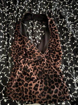 Leopardmönstrad halterneck topp - Snygg leopardmönstrad halterneck topp med djup v-ringning. Toppen har en brun bas med svarta leopardfläckar och är ärmlös. 