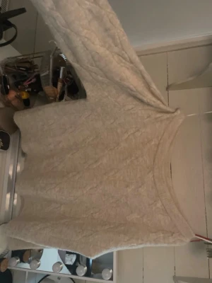 Beige kabelstickad tröja - Mysig beige kabelstickad tröja med rund halsringning och långa ärmar. Tröjan har ribbstickade muddar vid ärmslut och nederkant, vilket ger en klassisk och stilren look. Perfekt för kyligare dagar och enkel att matcha med olika outfits.