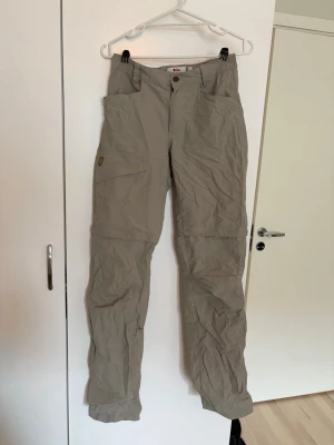 Fjällräven friluftsbyxor - Ljusgröna/gråa lite tunnare friluftsbyxor från Fjällräven. Det går att ta av en del av benet så att byxorna blir till shorts. 🌷