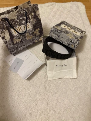 Svart bälte med logga  - Snyggt svart bälte med tydlig CD-logga framtill. Bältet har ett elegant mönster och levereras med originalpåse och ask. Perfekt accessoar för att lyfta din outfit.