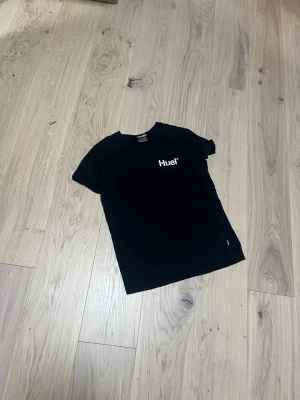 Svart Huel t-shirt i bomull - Snygg svart t-shirt från Huel med vit logga på bröstet. Inga större problem med den, tvättas innan leverans 