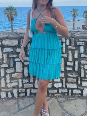 Turkos med volanger Zara - Säljer en turkos kortklänning med omlottdesign och volanger i flera lager. Klänningen har smala axelband och knytning i mitten som kan knytas på olika sätt. Perfekt för sommarens alla tillfällen!
