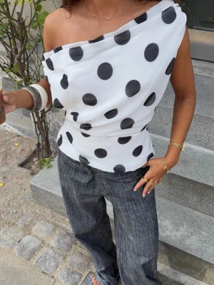 Prickig offshoulder topp i vitt och svart - Säljer en vit offshoulder topp med stora svarta prickar från DesignBySi.  Toppen har en asymmetrisk design. Aldrig använd och prislappen fortfarande kvar på tröjan. Skickar gärna mer bilder på förfrågan ☺️