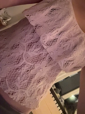 Ljusrosa spetsig linnetopp - Säljer en ljusrosa linnetopp med tunna axelband och vacker spets med blommönster. Toppen har en volangdetalj över bröstet och är perfekt för dig som gillar romantiska och feminina plagg. Materialet är mjukt och luftigt, vilket gör den skön att bära.