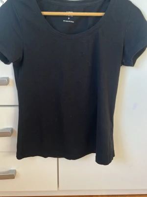 Svart basic t-shirt från Lager 157 - En enkel svart t-shirt från Lager 157 med rund halsringning och korta ärmar. Tillverkad i mjuk bomull som känns skön mot huden. Perfekt att matcha med jeans eller kjol för en clean och stilren look.