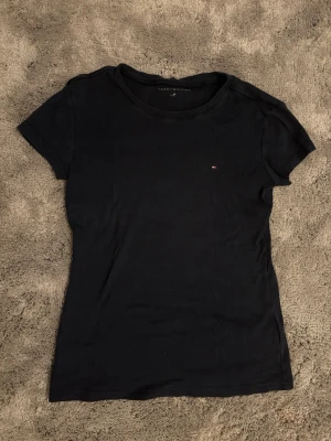 Mörkblå t-shirt från Tommy Hilfiger - Klassisk svart t-shirt från Tommy Hilfiger med liten broderad logga på bröstet. T-shirten har rund halsringning och korta ärmar. Perfekt basplagg i mjuk bomull som funkar till allt.