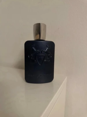 Parfums de Marly Layton 125ml - Mörkblå parfymflaska från Parfums de Marly med elegant silverfärgat lock. Flaskan har en matt finish och är dekorerad med två upphöjda hästar och en sköld med siffran 1743. Lyxig och stilren design som sticker ut i badrumshyllan.         HELT NY ENDAST TEST SPRUTAD 2 GÅNGER