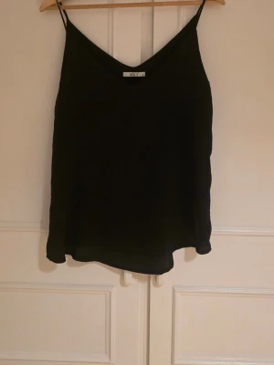 Svart linnetopp - Säljer en enkel och stilren svart linnetopp med tunna axelband och v-ringad hals. Aldrig använd