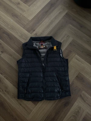 Svart dunväst från parajumper - Snygg svart dunväst från parajumper med quiltad design och dragkedja framtill. Västen har två fickor med dragkedja och en liten gul detalj vid kragen. Perfekt för lager-på-lager och streetstyle.