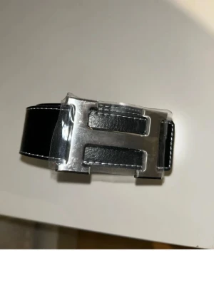 Svart skärp med stor H-spänne - Snyggt svart skärp  med ett stort, silverfärgat H-spänne. Pris kan diskuteras. Snabb affär-rabbat.