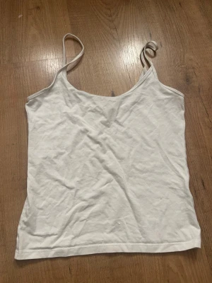 Vit enkel linnetopp med tunna band - Säljer en vit linnetopp med tunna axelband och rak passform. Toppen är ärmlös och har en mjuk, lätt känsla som passar perfekt till sommaren. Enkel och stilren design utan mönster eller detaljer.