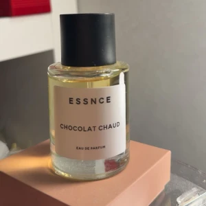 ESSNCE Chocolat Chaud parfym - ESSNCE Chocolat Chaud Eau de Parfum i en rund glasflaska med svart lock. Doften har en varm och söt karaktär inspirerad av varm choklad. Flaskan är transparent med en enkel vit etikett och svart text, vilket ger ett stilrent och modernt intryck. Sprayat ungefär 5 sprut