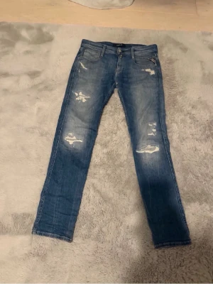 W29 L32 Blå slitna replay jeans - Säljer ett par blå jeans med slitningar och skinny passform. Jeansen har klassisk femficksdesign, normal midja och snygga slitdetaljer framtill. Perfekta för en avslappnad och trendig look.
