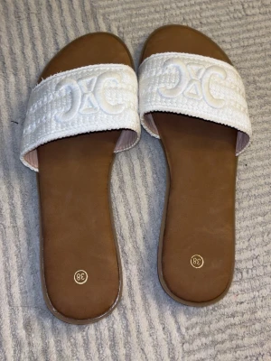 Vita slip-in sandaler med broderi - Vita slip-in sandaler med broderad detalj framtill och brun sula. Platt modell som är bekväm och enkel att bära. Perfekta för sommar, semester eller vardag. Oanvända, sulorna i fint skick.🖤