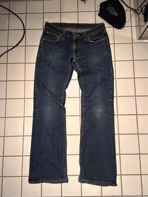Bootcut jeans från Nudie Jeans - Säljer ett par klassiska mörkblå jeans från Nudie Jeans med bootcut längst ner och snygga kontrastsömmar. Jeansen har fem fickor och detaljerade broderier på bakfickorna. Tillverkade i slitstark denim, perfekta för en avslappnad och stilren look. Bootcut Eddy W28/L30 För små för mig men skulle nog sitta bra på dig som är mellan 170-175