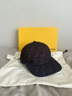 Svart keps med Fendi-logga - Snygg svart keps från Fendi med det klassiska FF-monogrammet över hela kepsen. Kepsen har böjd skärm och justerbar rem bak. Tillverkad i ett slitstarkt tyg som ger en exklusiv känsla. Perfekt accessoar för att lyfta din streetwear-look.