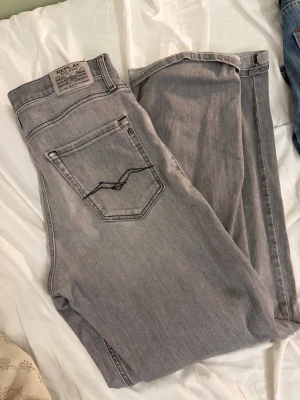 Grå Replay jeans - Säljer ett par snygga grå jeans från Replay med klassisk femficksmodell och raka ben. Jeansen har en ljusgrå tvätt och detaljerade sömmar på bakfickorna. Tillverkade i bomull med en skön passform. Perfekta till en avslappnad stil.