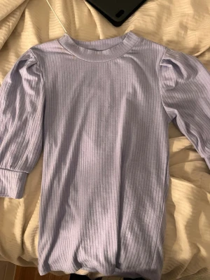 Ljuslila ribbad topp med puffärm - Säljer en ljuslila ribbad topp med puffärm och rund hals. Har använt minst 4 gånger. Perfekt att styla med jeans eller kjol för en trendig look.💕DM vid frågor/intresse!