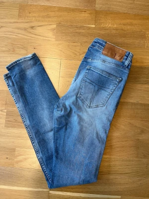 Blå slim jeans från tiger of Sweden - Säljer ett par klassiska blå slim jeans från tiger of Sweden. Jeansen har en snygg tvätt, fem fickor och läderpatch med logga bak i midjan. Perfekta till vardags och lätta att matcha med olika stilar.
