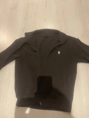 Svart zip hoodie från Ralph Lauren - Snabb leverans pris kan diskuteras. Säljer en svart hoodie med dragkedja från Ralph Lauren. Klassisk design med två fickor framtill och den ikoniska vita loggan broderad på bröstet. Tillverkad i mjukt bomullsmaterial och har ribbade muddar vid ärmslut och nederkant. Perfekt för en avslappnad stil.