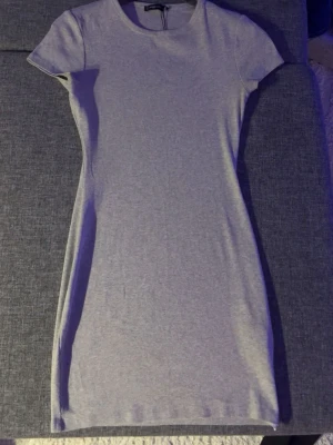 Ljusgrå ribbad kortklänning - En enkel och stilren ljusgrå kortklänning med ribbad struktur och rund hals. Klänningen har korta ärmar och en kroppsnära passform som framhäver siluetten. Perfekt att matcha med sneakers eller boots för en avslappnad look. Storlek l men passar från s till l 