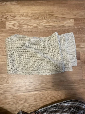 Beige stickad sjal i grovt garn - Mysig beige stickad sjal med grov struktur och ribbade kanter. Perfekt att svepa runt sig för extra värme. Enkel och stilren design som passar till många outfits.