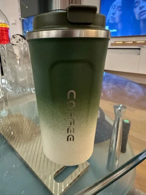 Grön termosmugg med temperaturdisplay - Säljer en snygg termosmugg i grön och beige färg med metallkant och digital temperaturdisplay i locket. Muggen har texten 'COFFEE' på sidan och är perfekt för att hålla drycken varm eller kall. Praktisk och stilren design för dig som är på språng. Finns en liten repa som syns på sista bilden🫶🏼